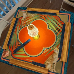 May include: A colorful Mahjong game table with a vibrant orange and teal floral design. The table features cheetah illustrations, wooden rails, and blue tile holders. The game is set up with tiles in place, ready for play.