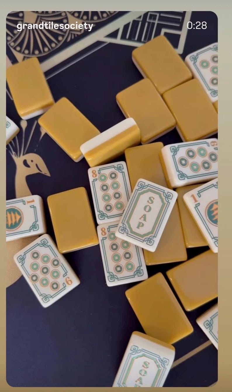 Puede incluir: Una colecci&oacute;n de fichas de Mahjong rectangulares con reverso amarillo mostaza y frente blanco. Algunas fichas presentan patrones circulares verdes y rojos, mientras que otras muestran la palabra SOAP en letras verdes. Las fichas est&aacute;n dispersas.