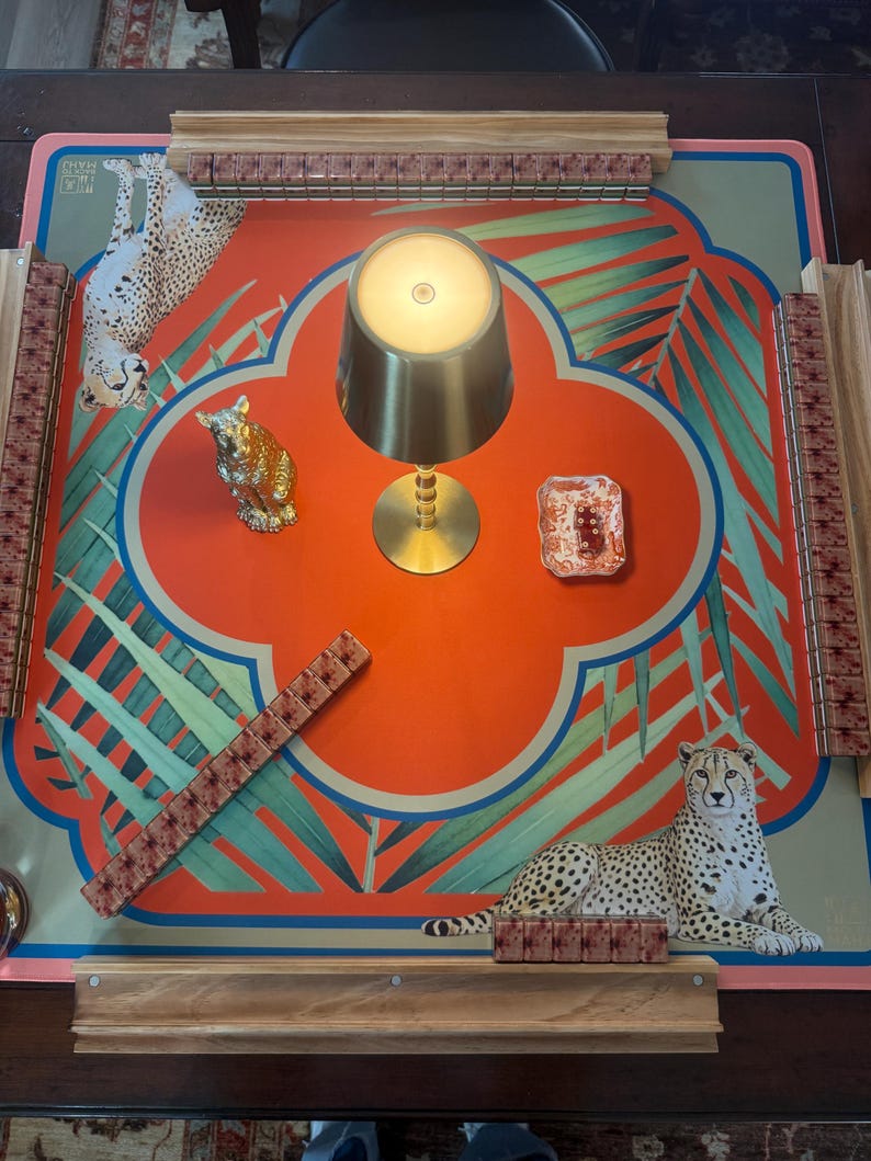 May include: A decorative game board with a vibrant orange and teal design featuring cheetahs and tropical foliage. Includes a gold-colored lamp, a small decorative dish, and a gold-colored cat figurine. The board has wooden rails and game pieces.