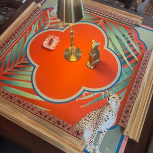 May include: A decorative Mahjong table with a vibrant orange and green floral design, featuring a cheetah illustration. Includes a gold lamp and a small gold cat figurine. The table has wooden edges and a patterned border.