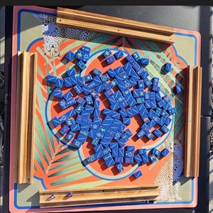 May include: A Mahjong set with blue tiles scattered on a colorful game board. The board features a tropical design with orange, green, and pink hues, and wooden tile holders. The board has a cheetah print border.