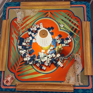 May include: A colorful Mahjong game set with a vibrant orange and teal design. The game board features a cheetah illustration and palm fronds. The set includes blue and white tiles, a small gold figurine, and a decorative lamp.