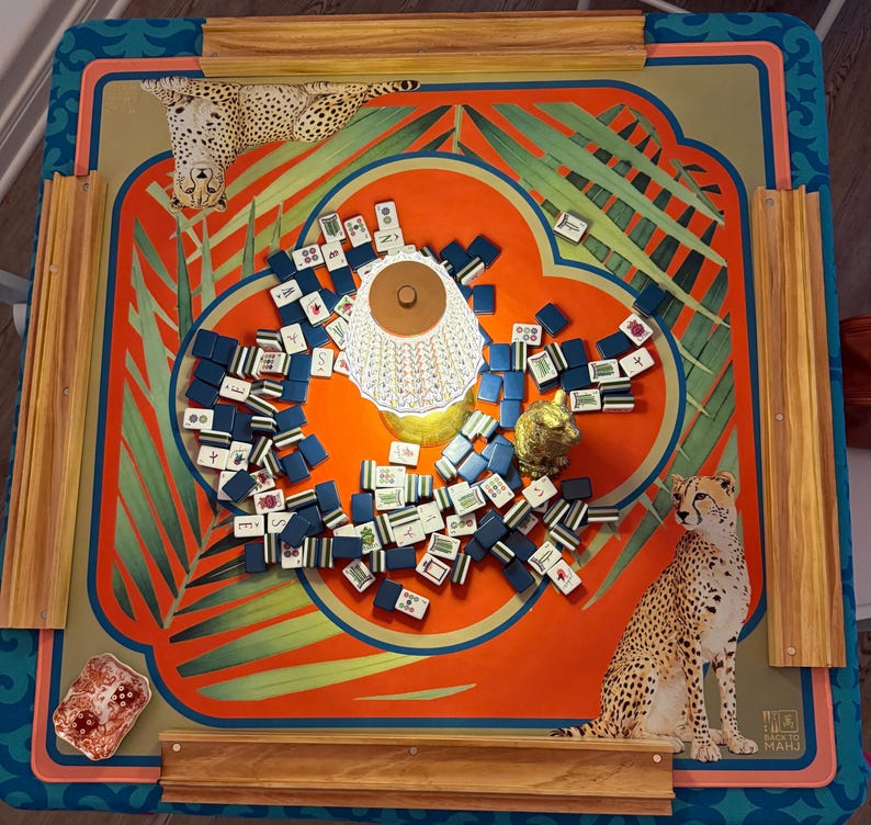 May include: A colorful Mahjong game set with a vibrant orange and teal design. The game board features a cheetah illustration and palm fronds. The set includes blue and white tiles, a small gold figurine, and a decorative lamp.