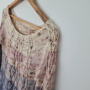 May include: A knitted sweater with a cable knit pattern in shades of cream, pink, and purple.
