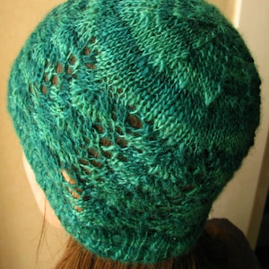 May include: A green knitted hat with a lacy pattern. The hat is made of a soft, textured yarn.