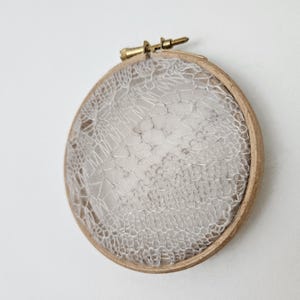 Op de afbeelding: Een wit kantontwerp is gespannen in een ronde houten borduurring.