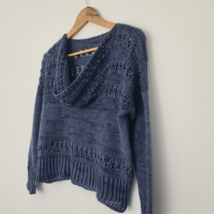 Könnte beinhalten: Ein blauer Strickpullover mit einem Rollkragen und durchbrochenen Details. Der Pullover hat lange Ärmel und einen verkürzten Saum.