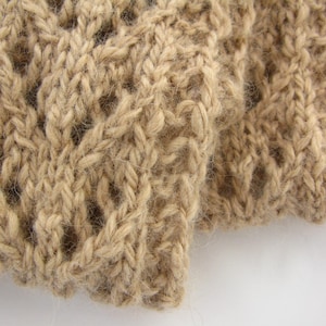 May include: Close-up of a tan knitted fabric with a textured, openwork design. The yarn appears to be a soft, natural fiber, creating a cozy and warm aesthetic. The knitting pattern features a repeating cable and open stitch design.