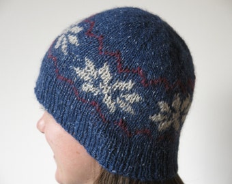 May include: A blue knitted hat with a white and red patterned design. The hat has a snowflake pattern.