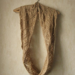 May include: A tan knitted scarf with a simple, openwork design hangs on a wooden hanger.