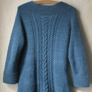 Könnte beinhalten: Ein blauer Strickcardigan mit einem Zopfmuster auf der Rückseite. Der Cardigan hat lange Ärmel und einen V-Ausschnitt.
