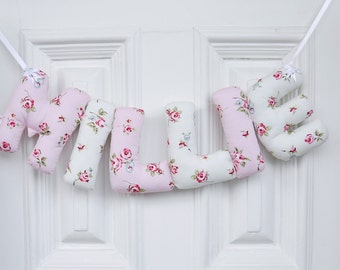 May include: A pink and white floral fabric banner spelling out the name "MILLIE".