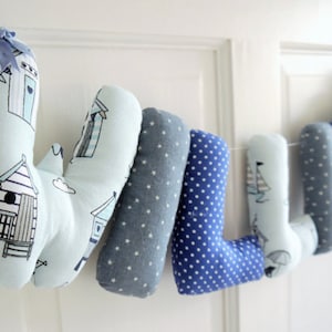 May include: A blue and white fabric letter banner spelling the name "WILLIE". Each letter is a separate pillow with a different pattern. The letters are connected with a white string.