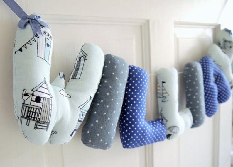 May include: A blue and white fabric letter banner spelling the name "WILLIE". Each letter is a separate pillow with a different pattern. The letters are connected with a white string.