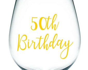Puede incluir: Una copa de vino de vidrio transparente con una calcomanía de vinilo dorado que dice "50th Birthday".