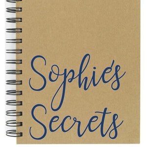 Peut inclure: Un carnet à spirales marron avec le texte "Sophie's Secrets" en écriture cursive bleue.