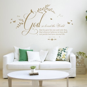 Puede incluir: Un sofá blanco con almohadas de estampado floral y verde en un ambiente de sala de estar. Un adhesivo de pared con el texto "For God so loved the World that he gave his one and only Son, that whoever believes in him shall not perish but have eternal life. John 3:16" se muestra en la pared.