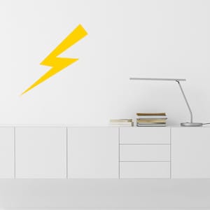 May include: A white cabinet with three doors and three drawers, a desk lamp, and a yellow lightning bolt sticker on the wall above the cabinet.