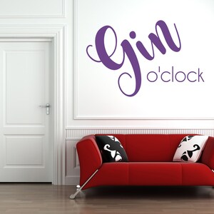 May include: A red couch with two pillows in a white room with a white door and a purple wall decal that says "Gin o'clock".