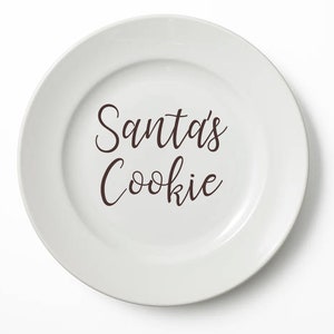 Peut inclure: Assiette en céramique blanche avec le texte "Santa's Cookie" écrit en cursive brune.
