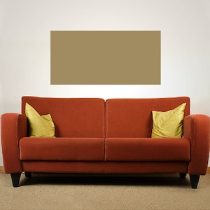 Op de afbeelding: Een rode bank met twee gele kussens staat voor een beige muur met twee zwarte wandlampen met witte lampenkappen.