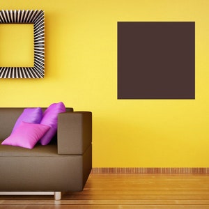 Könnte beinhalten: Ein braunes Sofa mit drei lila Kissen vor einer gelben Wand. Ein schwarzes gerahmtes Bild hängt an der Wand über dem Sofa. Der Boden ist aus Holzdielen.