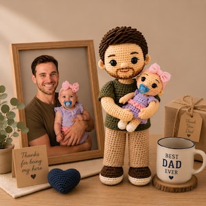 May include: A crocheted doll of a man holding a crocheted baby doll, a framed photo of a man and baby, a mug that says "BEST DAD EVER", a gift box, a blue heart, and a card that says "Thanks for being my hero".