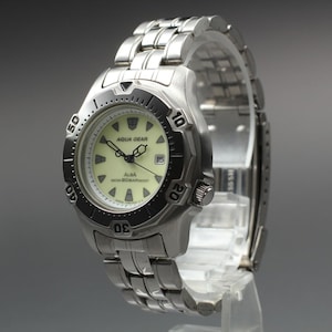 May include: A stainless steel wristwatch with a silver link bracelet and a round case. The watch features a pale yellow dial with black hands, hour markers, a date window, and the text Aqua Gear and Alba Water 20BAR Resist on the face.