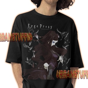 May include: Black t-shirt featuring a graphic from "Ergo Proxy" with a female character in a dark outfit. The shirt has the text "Ergo Proxy" in white. The model is wearing blue jeans.