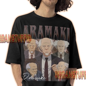 May include: Black t-shirt featuring a graphic of a man in a suit with the name "ARAMAKI" above the image and the name "Daisuke" below. The shirt has a vintage style.