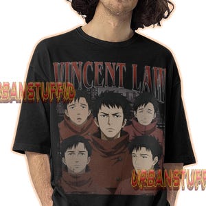 May include: Black t-shirt with a graphic of anime characters and the text "VINCENT LAW" in red. The shirt also has the text "URBANSTUFFID" in orange. The t-shirt is worn by a person.