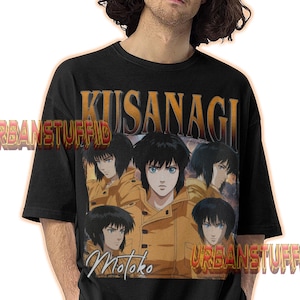 May include: Black t-shirt featuring a graphic of a character from the anime series, "Ghost in the Shell." The design includes the name "Kusanagi" and the name "Motoko." The shirt also has the text "URBANSTUFFID" printed on it.