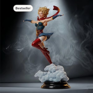 May include: A figurine of a woman in a superhero costume, with a blue and red color scheme. The figure is posed mid-air, with a red cape flowing behind her. The base is a cloud-like structure. The word "Bestseller" is in a white oval.
