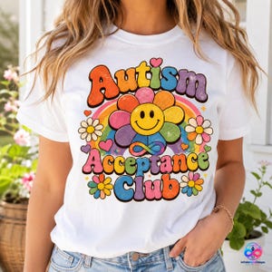 以下が含まれることがあります： 「Autism Acceptance Club」というレトロなフォントのテキストが描かれた、カラフルなグラフィック付きの白いTシャツ。デザインには、中央のスマイリーフェイスの花、虹、小さなデイジー、ハート、そして鮮やかな色の無限大のシンボルが含まれています。