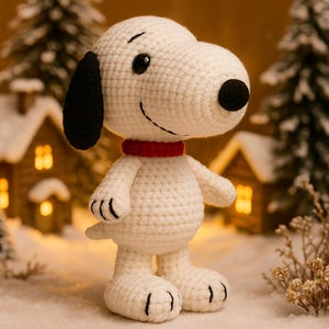 May include: A crocheted Snoopy figure, featuring the iconic white dog with black ears, nose, and a red collar. The figure is set in a snowy scene with miniature houses and evergreen trees, evoking a winter theme. The figure is handmade.