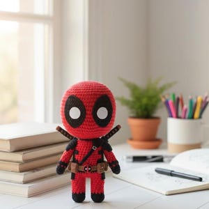 May include: A handmade crochet Deadpool doll in a standing pose. The doll is primarily red with black accents, including a mask with large white eyes. It has a utility belt and two katana swords on its back. The doll is approximately 7 inches tall.