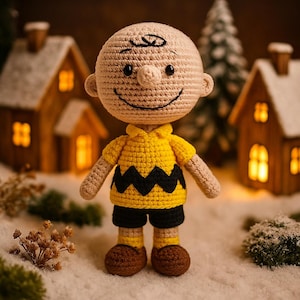 Puede incluir: Muñeco de ganchillo hecho a mano de un personaje de dibujos animados, que lleva una camisa amarilla con un diseño de zigzag negro, pantalones cortos negros y zapatos marrones. El muñeco tiene una cara sonriente y está ambientado en un fondo nevado con casas en miniatura y un árbol de Navidad.