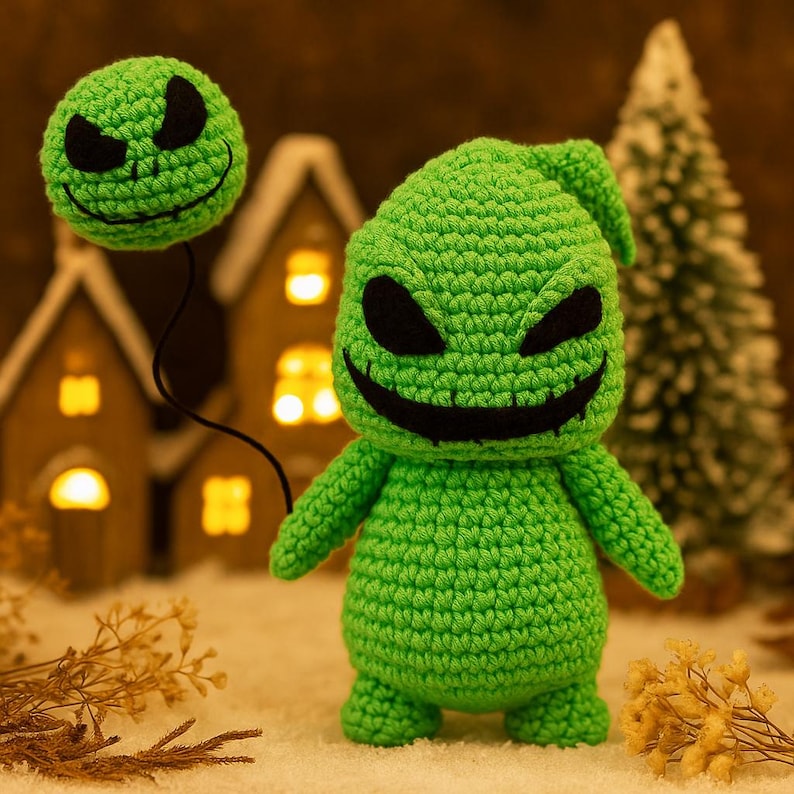 Może przedstawiać: Ręcznie robiona zielona lalka Oogie Boogie na szydełku z czarnymi oczami i wyszytym uśmiechem. Mniejsza, odłączona głowa unosi się nad nią, połączona czarnym sznurkiem. Lalka jest umieszczona na rozmytym tle z miniaturowymi domkami i choinką.