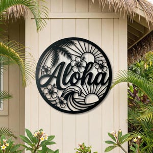 Könnte beinhalten: Runde Wandkunst aus schwarzem Metall mit dem Wort "Aloha". Das Design umfasst Palmen, Hibiskusblüten, eine Sonne und Wellen. Das Kunstwerk ist an einer hellen Wand angebracht, umgeben von tropischen Pflanzen.