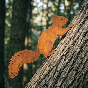 May include: A rusty brown metal squirrel climbing a tree. The squirrel has a long, bushy tail and is attached to the tree trunk. The background is blurred, showing a forest setting.