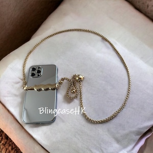 May include: A silver smartphone with a gold chain strap. The phone case features a gold wave design. The chain is a woven style with an adjustable section. The text "BlingcaseHK" is visible on the phone.