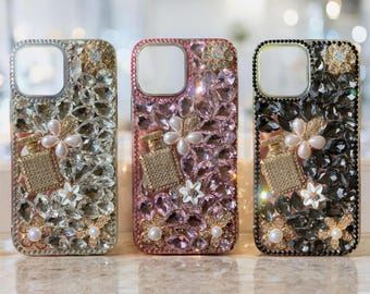 Op de afbeelding: Drie versierde telefoonhoesjes in zilver, roze en zwart. Elke hoes heeft een parfumflesontwerp, bloemaccenten en parelversieringen. De hoesjes zijn ingelegd met sprankelende kristallen.