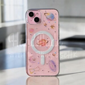 Könnte beinhalten: Eine rosa Handyhülle mit Weltraum-Motiv. Die Hülle zeigt Illustrationen von Planeten, Sternen und Sternbildern. Sie hat einen transparenten Rand und den Text "Handmade with BlingcaseHK".