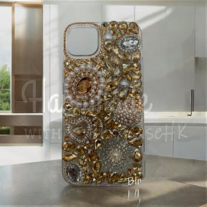 Op de afbeelding: Transparante telefoonhoes versierd met gouden en heldere strass, parels en een gouden rand. De hoes heeft verschillende vormen en maten strass, wat een luxueuze en glamoureuze uitstraling creëert. De tekst "Hala with Bling seHK" is zichtbaar.
