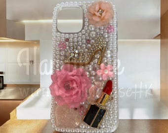 Op de afbeelding: Decoratieve telefoonhoes met parels, met een met strass bezette high-heel schoen, roze stoffen bloemen en een lippenstift. De hoes heeft een uitsparing voor de camera. Het ontwerp is vrouwelijk en glamoureus.