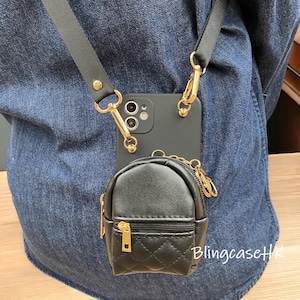 May include: Black phone case with a detachable black strap and gold-colored hardware. A small, black, quilted backpack-shaped pouch is attached to the phone case. The text "BlingcaseHK" is visible on the lower right.