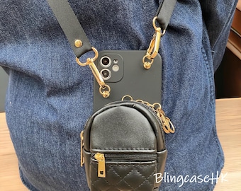 Puede incluir: Funda de teléfono negra con una correa negra desmontable y herrajes dorados. Una pequeña bolsa negra acolchada con forma de mochila está sujeta a la funda del teléfono. El texto "BlingcaseHK" es visible en la parte inferior derecha.