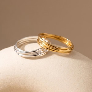 May include: Two interlocking rings, one crafted from polished silver-tone metal and the other from gold-tone metal. Each ring features a smooth, rounded band design, with the two pieces resting together to form a cohesive, layered jewellery set.