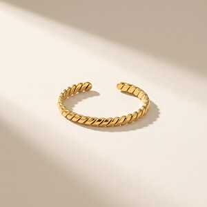 Peut inclure: Un bracelet ouvert doré présentant une texture torsadée en forme de corde continue. Le bracelet circulaire possède une finition métallique polie et un petit espace entre les deux extrémités, créant un design flexible au motif en spirale.