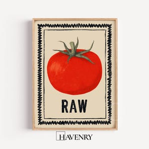 May include: A framed print featuring a vibrant red tomato with green stem and the word "RAW" in bold black letters. The tomato illustration is set against a beige background, framed by a black zigzag border.